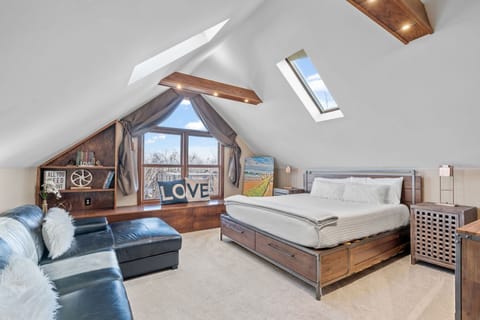 Unwind in your cozy attic retreat with skylights bringing in natural light, comfortable seating, and warm wood details.