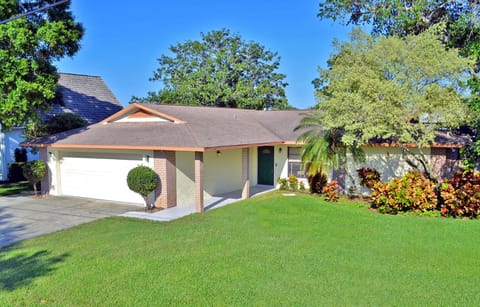 Ranch-style home exterior with large oak tree, attached garage, and tropical landscaping