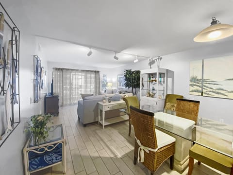 Bright living room with dining area, light gray sofas, coastal blue wall art, and wood-look flooring