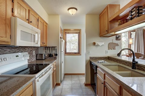 A compact kitchen with wooden cabinets, white appliances, a granite countertop, a window, and a double sink. Kitchen utensils are organized and stored neatly.
