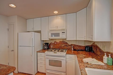 A kitchen with white cabinets, a white refrigerator, and a white stove with an overhead microwave. Countertops are granite, and a coffee maker, toaster, and soap dispensers are present.