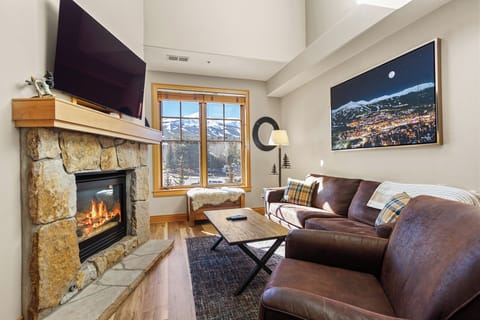 Cozy up by your stone fireplace while enjoying mountain views through expansive windows in this inviting living space.