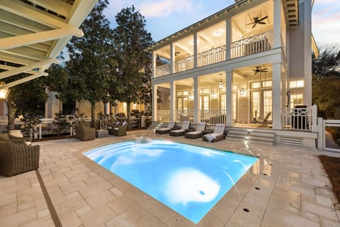 Luxurious coastal-style property with illuminated swimming pool and spacious covered porches, perfect for evening relaxation.