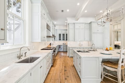 Step into your dream kitchen with pristine white cabinetry, marble countertops, and warm hardwood floors beneath an elegant chandelier.