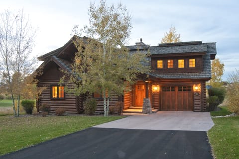 Step into your own rustic mountain retreat! This charming log home glows warmly at dusk, surrounded by peaceful autumn trees and manicured lawns that invite evening strolls.