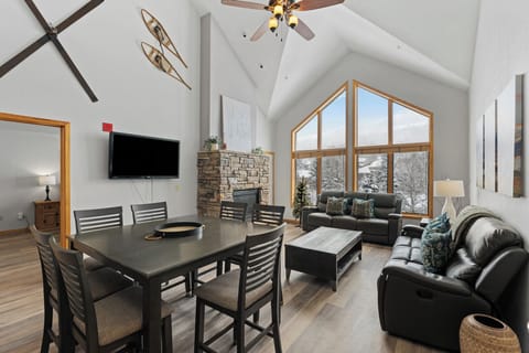 Unwind in your spacious living area with vaulted ceilings, where a stone fireplace radiates warmth and floor-to-ceiling windows frame serene snowy forest views—your perfect mountain retreat.