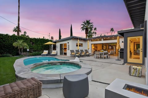 Modern outdoor paradise with sparkling pool, hot tub, and cozy fire pit under a stunning sunset sky.