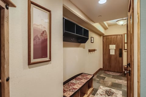 A hallway with a bench, coat hooks, a framed picture on the wall, and a door leading outside.