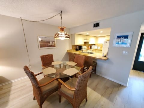Bright dining space with woven chairs and open-plan kitchen view.