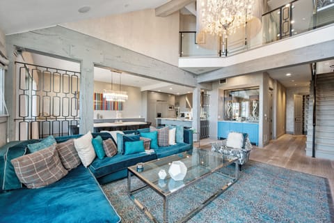 Relax in this stunning open-concept living space featuring plush teal velvet seating, elegant crystal chandeliers, and soaring ceilings that create an airy, luxurious atmosphere.
