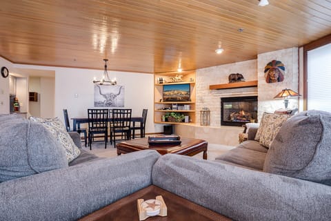Gather around the warm stone fireplace in your spacious living area, complete with plush seating and rustic wood beam ceiling.