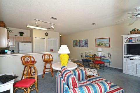 Relax in your open-concept retreat with colorful striped seating, full kitchen, and vibrant coastal artwork creating a cheerful beachside atmosphere.