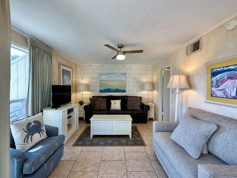 Sink into comfortable seating with coastal artwork and ceiling fan keeping you cool in this beach-themed living space.