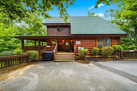 A charming log cabin nestled among lush greenery, offering a peaceful woodland retreat with convenient parking and a welcoming covered porch area.