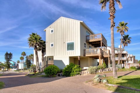 Modern beachside property with multiple balconies surrounded by swaying palm trees and manicured landscaping in a coastal neighborhood.