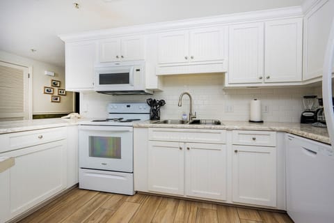 Prepare meals in the bright kitchen featuring white cabinetry, granite countertops, and white appliances
