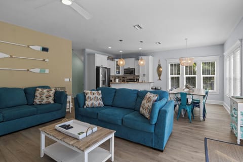Relax into plush teal sofas while enjoying your open-concept living space, complete with modern kitchen and bright dining area.