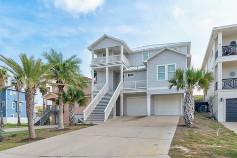 Coastal vacation home featuring elevated design with covered parking and tropical palm landscaping in a beach community setting.