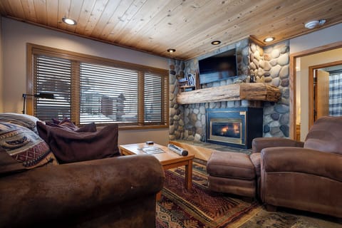 Cozy up by your stone fireplace in this warm living room featuring rustic charm and mountain views.