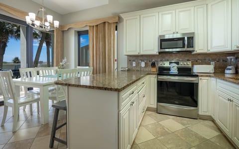 Dining area features a white table with matching chairs, complemented by a view of palm trees and the outdoors