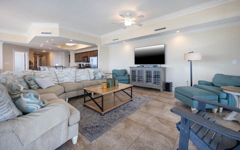 The living area features a large sectional sofa, a flat-screen TV, and a view into the modern kitchen, perfect for relaxation