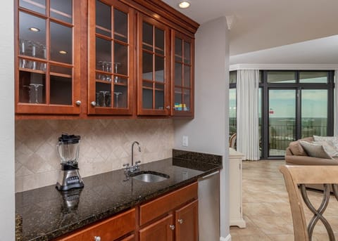 This wet bar features rich wood cabinetry, a sleek granite countertop, blender, and a view of the inviting living area