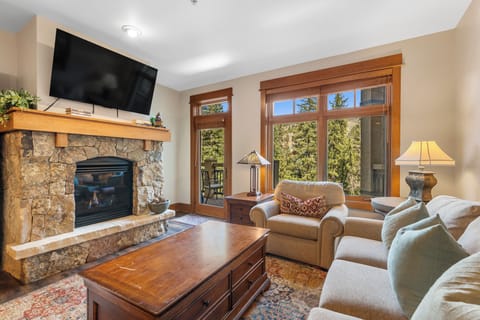 Unwind in your cozy living room with mountain views, where a crackling stone fireplace and plush seating invite you to relax after exploring the slopes.