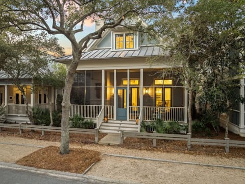 Charming cottage-style home with screened porch and metal roof nestled among mature oak trees in a peaceful neighborhood setting.