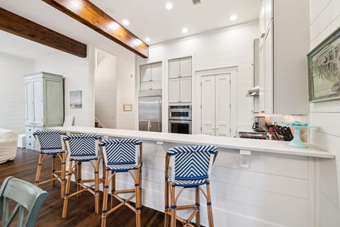Gather around your stylish kitchen island featuring coastal charm with navy chevron stools and warm wood beams overhead.