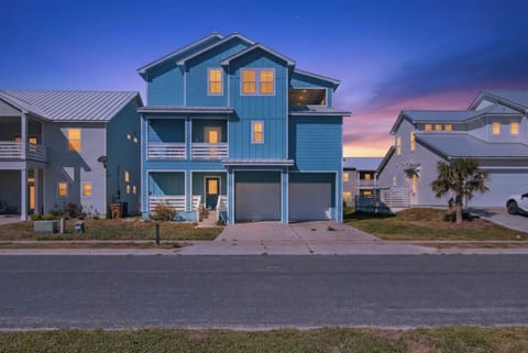Stunning blue beach house with warm lights glowing against the twilight sky in a modern coastal neighborhood.