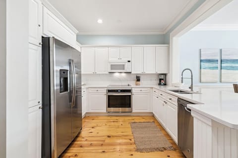 Your bright, fully equipped kitchen welcomes you with gleaming appliances and coastal charm—perfect for preparing meals with ocean-inspired artwork.