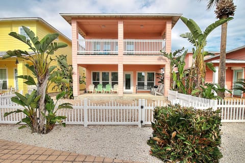 Charming coral-pink beach house with covered balcony and tropical landscaping in a colorful coastal neighborhood.