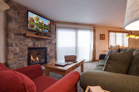 Cozy up in your warm living room featuring a crackling stone fireplace, plush seating, and entertainment for perfect relaxation.