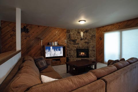 Cozy up in your rustic living room where warm wood walls meet a crackling stone fireplace, perfect for mountain evenings.