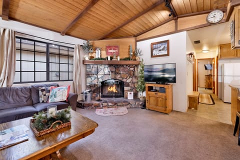 Cozy mountain living room with vaulted wood ceilings, stone fireplace, comfy seating, and smart TV—perfect for relaxing evenings, movie nights, and warm cabin vibes after outdoor adventures.