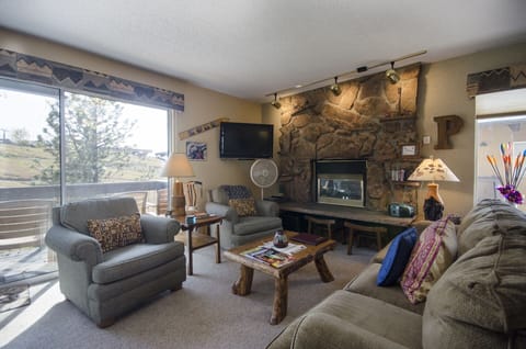Unwind in your cozy living room featuring a stunning stone fireplace, comfortable seating, and peaceful mountain views from the large windows.