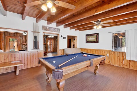 Rustic mountain cabin game room with a full-size pool table, exposed wood beams, cozy seating, and warm natural light—perfect for relaxing nights, friendly games, and unforgettable cabin stays.