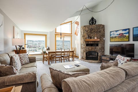 Unwind in your spacious living room featuring plush sectional seating, cozy stone fireplace, and panoramic windows framing stunning valley views.