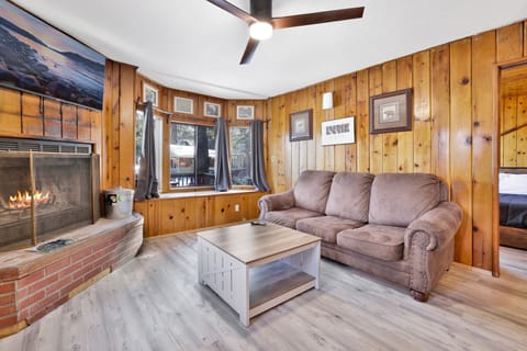 Cozy cabin living room with a stone fireplace, comfy seating, and rustic wood details—perfect for relaxing evenings, movie nights, and unforgettable mountain getaways.