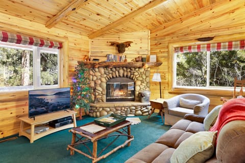 Cozy cabin living room with a stone fireplace, comfy seating, and a TV—perfect for relaxing evenings, movie nights, and unforgettable mountain getaways.