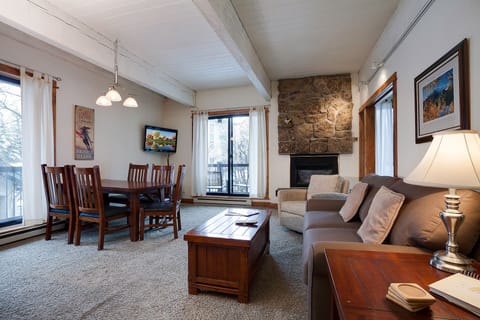 Relax in your spacious living room featuring a cozy stone fireplace, comfortable seating, and rustic wood beams overhead.