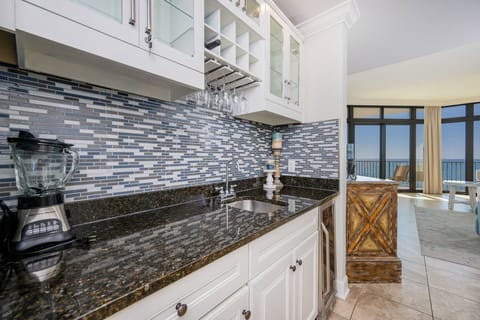 Stylish kitchen wet bar featuring sleek granite countertops, wine cooler, blender, and stunning balcony view