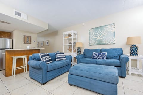 The living area features plush blue seating, coastal decor, and a convenient bar area for relaxation and entertainment
