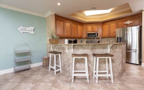 This kitchen features wood cabinetry, granite countertops, and a breakfast bar with three stools, perfect for morning coffee