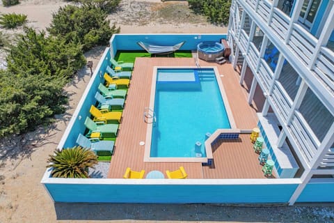 Aerial view of the vacation rental property featuring a sparkling swimming pool surrounded by colorful lounge chairs, a hot tub, and natural coastal landscape.