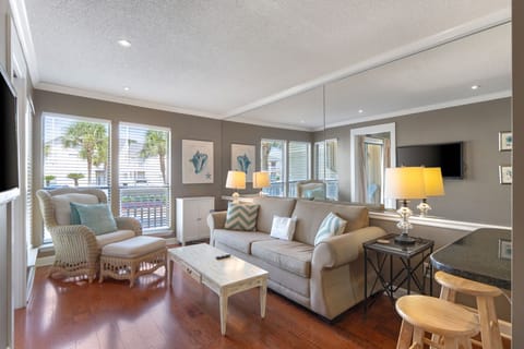 Relax in your coastal-themed living room with comfortable seating, warm lighting, and glimpses of palm trees through large windows.