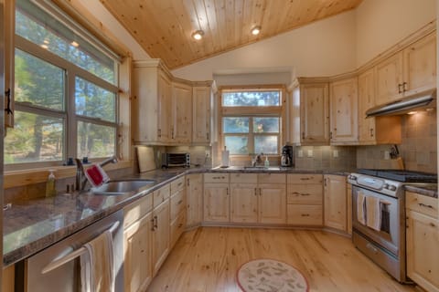 A spacious kitchen with wooden cabinets, a U-shaped counter, stainless steel appliances, and large windows overlooking trees.