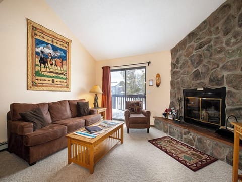 Cozy up in your mountain retreat with plush seating, stone fireplace warmth, and peaceful balcony views of snowy peaks.