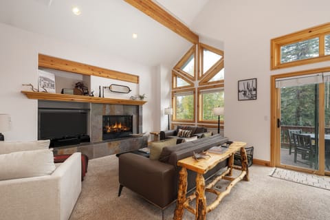 Relax in your spacious living room featuring soaring ceilings, a cozy fireplace, and floor-to-ceiling windows that flood the space with natural light.