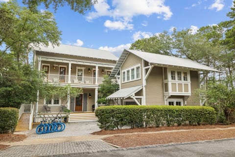 A charming two-story coastal home with double-wrap porches, bicycle parking, and lush landscaping welcomes guests to a peaceful neighborhood retreat.